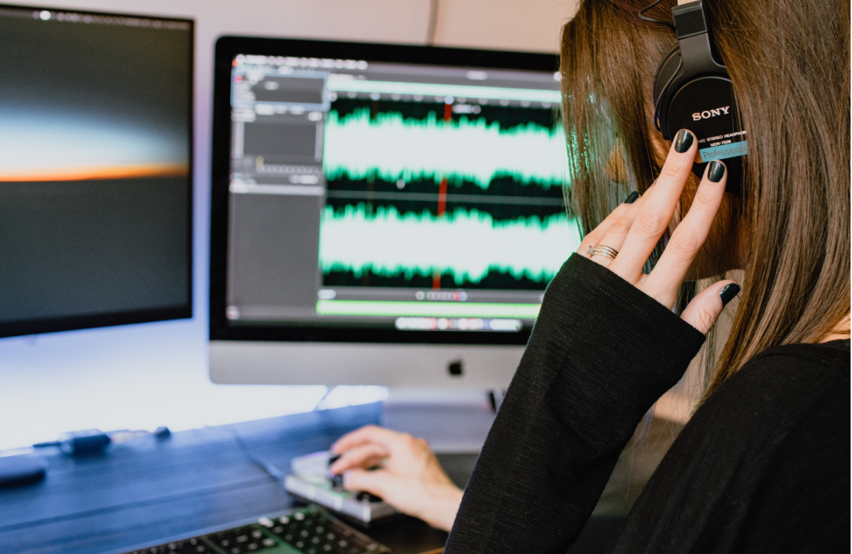 back of the head of a women with black fingernails - sitting in front of a monitor editing sound