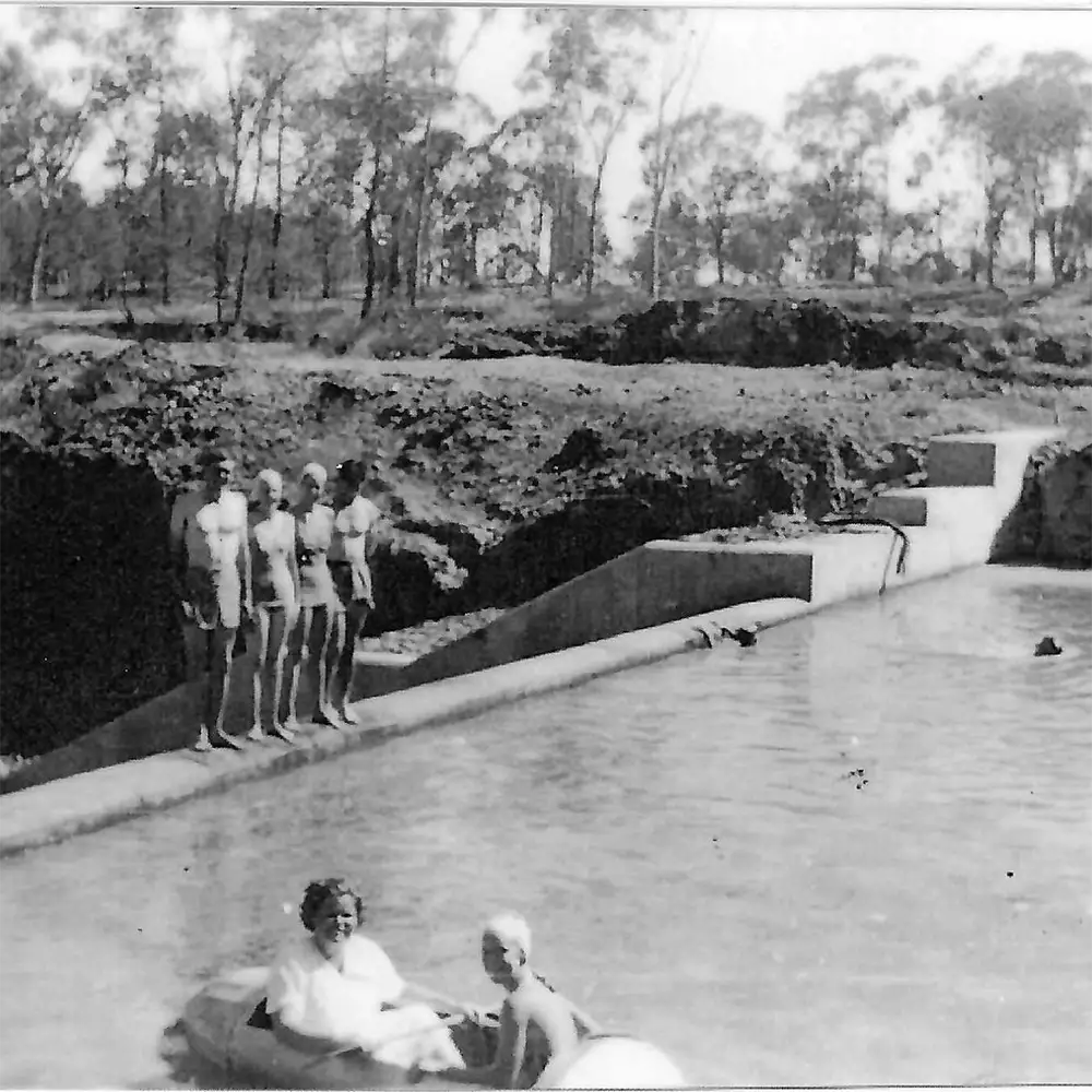 vintage photo of four people in swimming costumes at the edge of a concrete weir. Two women in a blow up dingy.