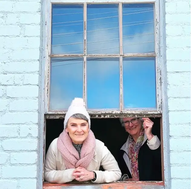 Two warmly dressed women looking out an old fashioned sash window