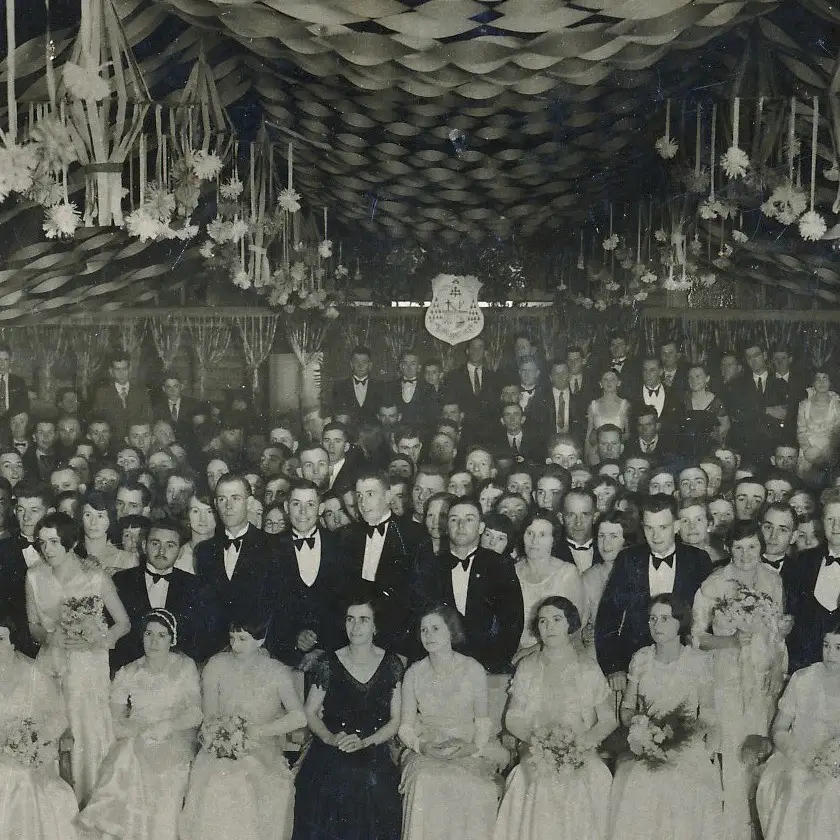 Vintage black and hite photo of a ball room with lots of women and men in ball room get-up. Gloriously festive.