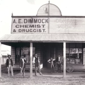 historic black and white image of men in front of chemist and faded sign of dental rooms - main street Nanago