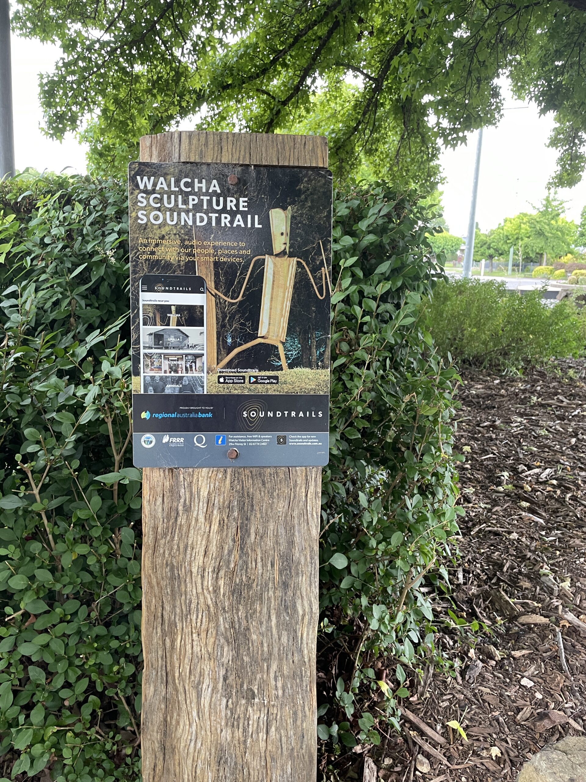 Large wooden post with a sign for the Walcha Sculpture Walk displaying a wooden sculpture and text.