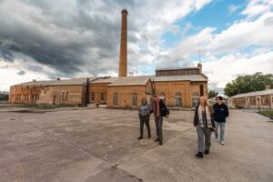 Four people listening to their mobile phones in front of a large industrial building