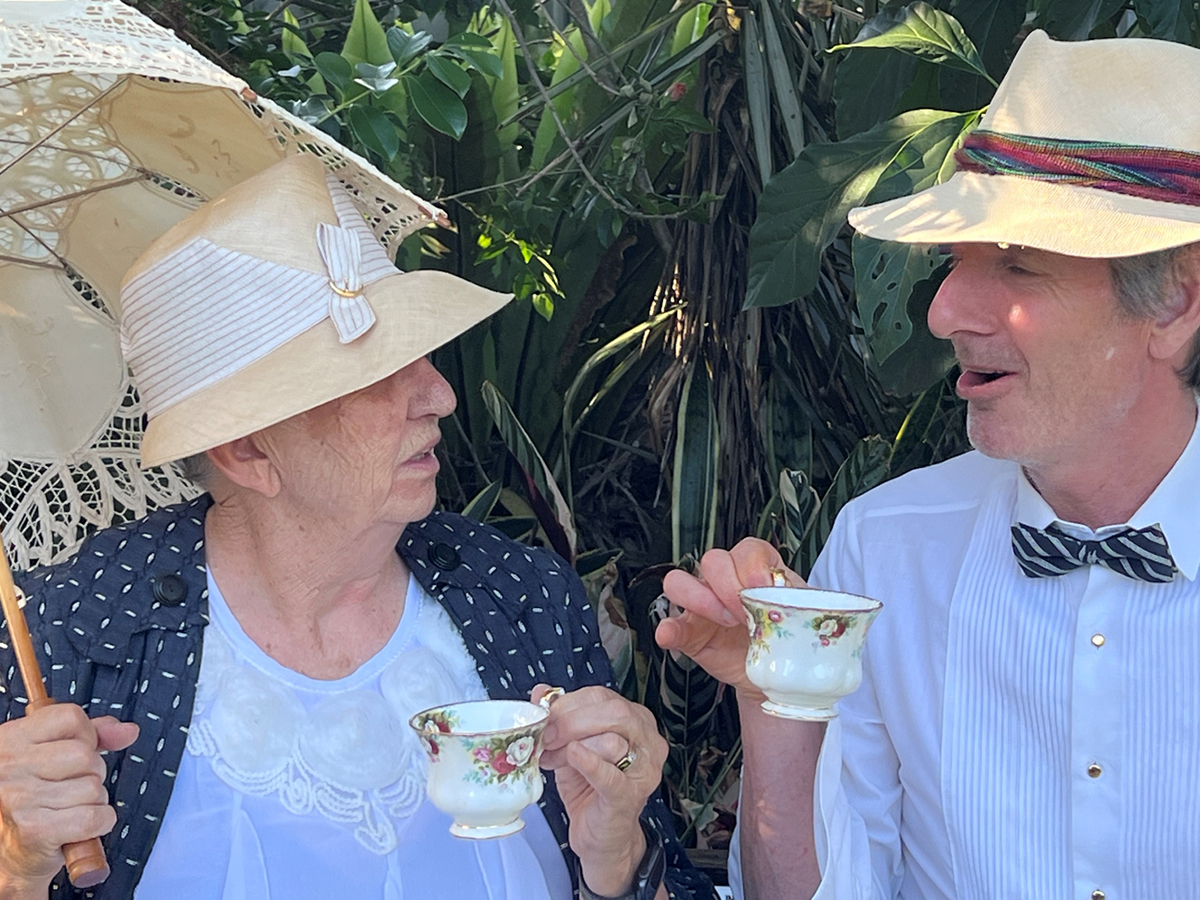 Man and woman dressed in 1920s costumes drinking tea outside