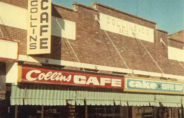oldfashioned colour photo of a row of shops in Nambour. Signs saying 'Collins Cafe' and 'cake'.